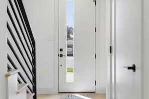 A hallway with a white door, a black and white striped wall, and a view of the outside. - Grand 3BR/3.5BA w/2-Car Garage mins to Downtown (Houston)