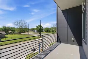 A balcony with a metal railing, a concrete floor, and a view of a green landscape with trees and a road. - Grand 3BR/3.5BA w/2-Car Garage mins to Downtown (Houston)