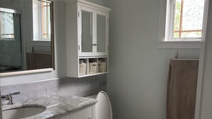 Ein Badezimmer mit Toilette, Waschbecken, Spiegel und einer Kommode mit Körben.