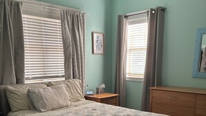 Ein Schlafzimmer mit einem Bett, einem Nachttisch, einer Kommode und einem Fenster mit Vorhängen.