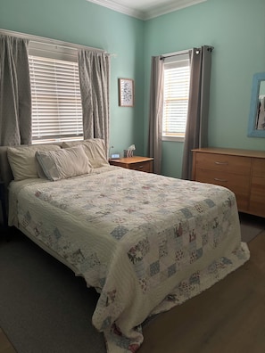 Een slaapkamer met een bed, nachtkastje, dressoir en een raam met gordijnen.