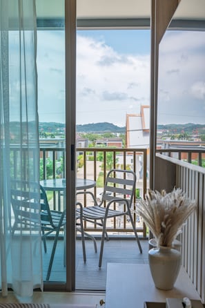 Ein Balkon mit Blick auf eine Wohngegend und Hügel, ausgestattet mit einem Tisch, Stühlen und einer Vase mit Trockenpflanzen.