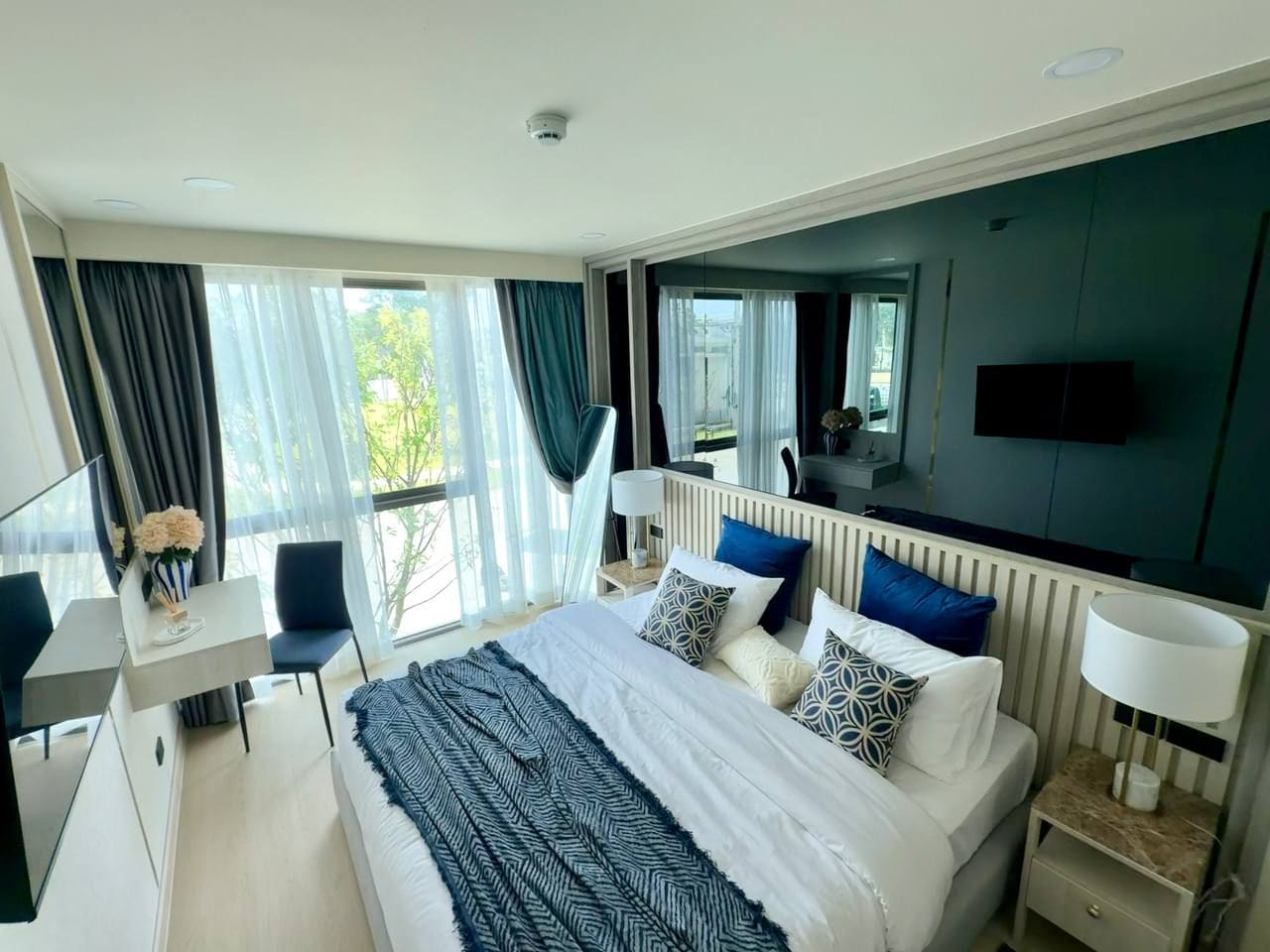A modern hotel room with a large bed, bedside tables, a desk, and a TV.