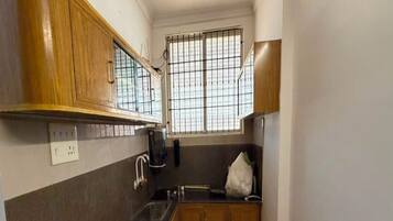 A narrow kitchen with wooden cabinets, a black countertop, a window with bars, and a white bag on the counter.
