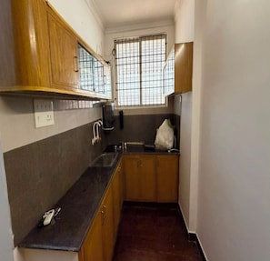 Una cocina estrecha con armarios de madera, una encimera negra, una ventana con rejas y una bolsa blanca sobre la encimera.