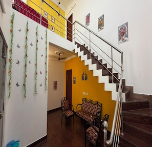 Una escalera con barandilla metálica que lleva a una zona de descanso con dos sillones estampados y una pared decorada con guirnaldas colgantes y adhesivos con forma de mariposas.