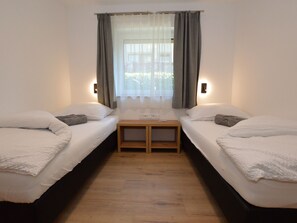 A room with two single beds, a small wooden table, and a window with curtains. - Modern, spacious apartment by the leisure lake (Uttendorf)
