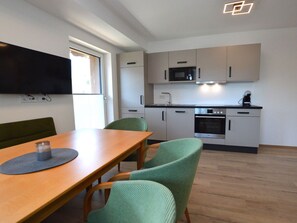 A modern kitchen with a dining area, including a table, chairs, and a TV mounted on the wall. - Modern, spacious apartment by the leisure lake (Uttendorf)