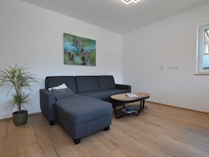 Ein modernes Wohnzimmer mit einem grauen Sofa, einem kleinen runden Tisch und einer Topfpflanze.