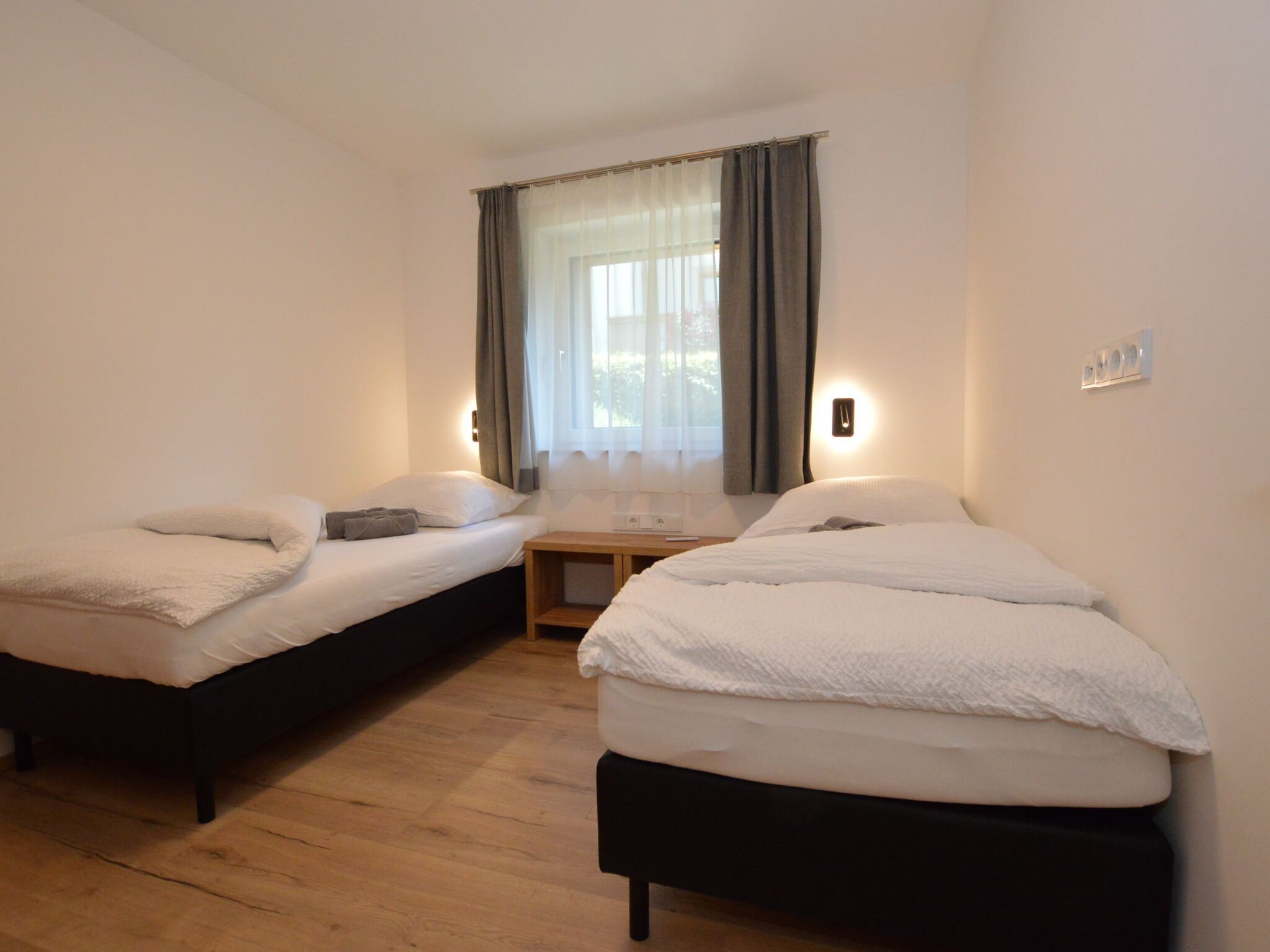 Une chambre avec deux lits simples, une petite table et une fenêtre avec des rideaux.