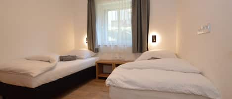 Ein Zimmer mit zwei Einzelbetten, einem kleinen Tisch und einem Fenster mit Vorhängen.