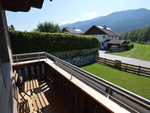 Ein Balkon mit Holzdeck und Metallgeländer, der auf ein Wohngebiet mit Häusern und Bergen im Hintergrund blickt.