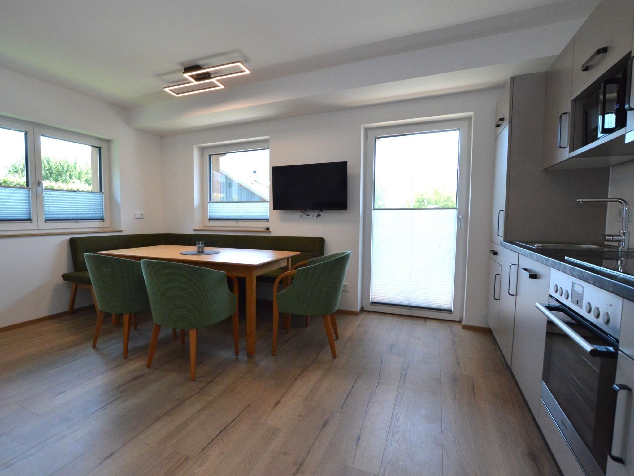 A modern kitchen with a built-in oven, a dining area with a table and chairs, and a flat-screen TV mounted on the wall.