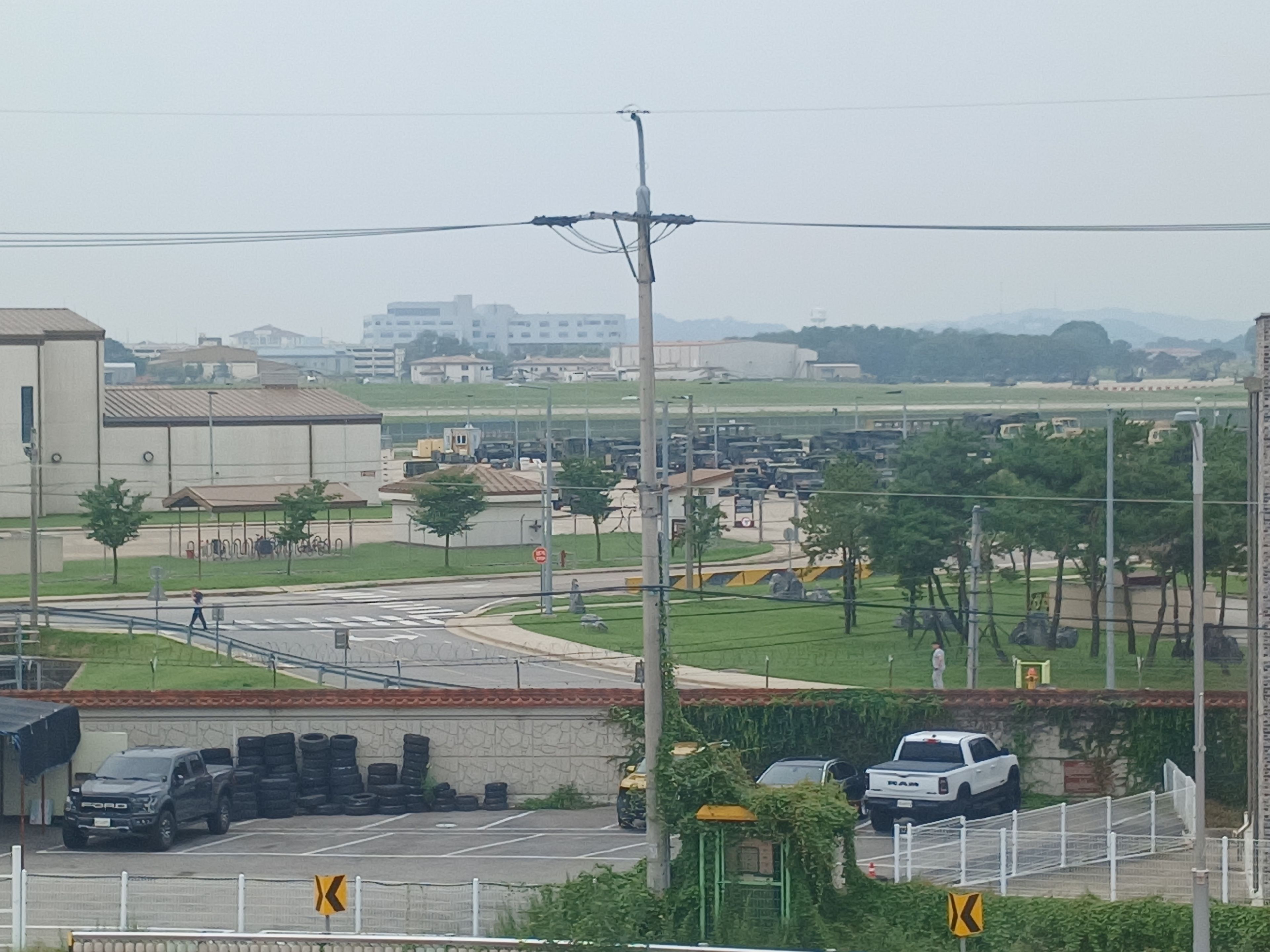 A parking lot with vehicles, a building with a flat roof, and a grassy area with trees.