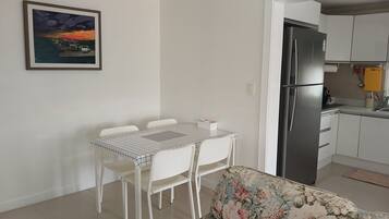 A dining area with a table and chairs, a sofa, a refrigerator, and a kitchen area with cabinets and a sink.