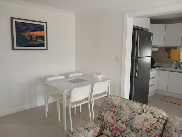 Un comedor con mesa y sillas, un sofá, un refrigerador y una zona de cocina con armarios y un fregadero.