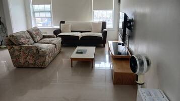 A living room with a sofa, a coffee table, a TV, and a fan.