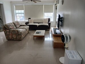 Ein Wohnzimmer mit einer Couch, einem Couchtisch, einem Fernseher und einem Ventilator.