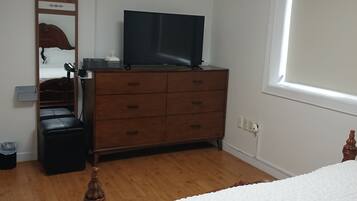 A bedroom with a bed, a dresser, a television, a ceiling fan, and a window.