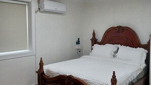Un dormitorio con una cama de madera, ropa de cama blanca, un ventilador de techo, un aire acondicionado y una ventana con persianas.
