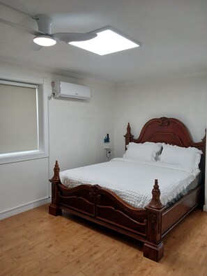 Ein Schlafzimmer mit einem hölzernen Bett, weißer Bettwäsche, einem Deckenventilator, einer Klimaanlage und einem Fenster mit Jalousien.
