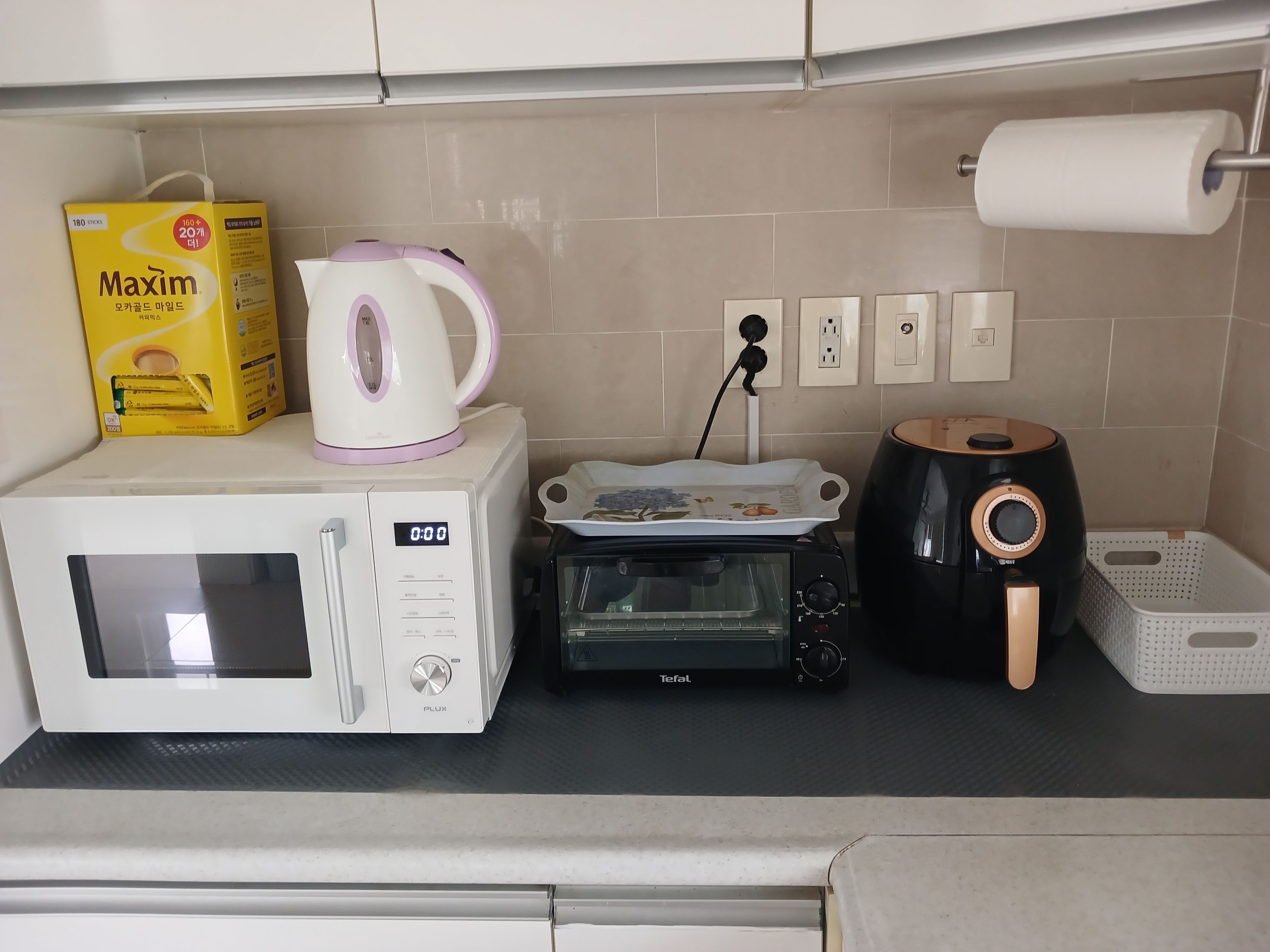 A kitchen with a microwave, toaster, kettle, and a box of Maxim tissues.