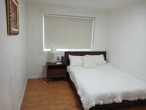 A bedroom with a bed, a nightstand, a lamp, a fan, and a window.