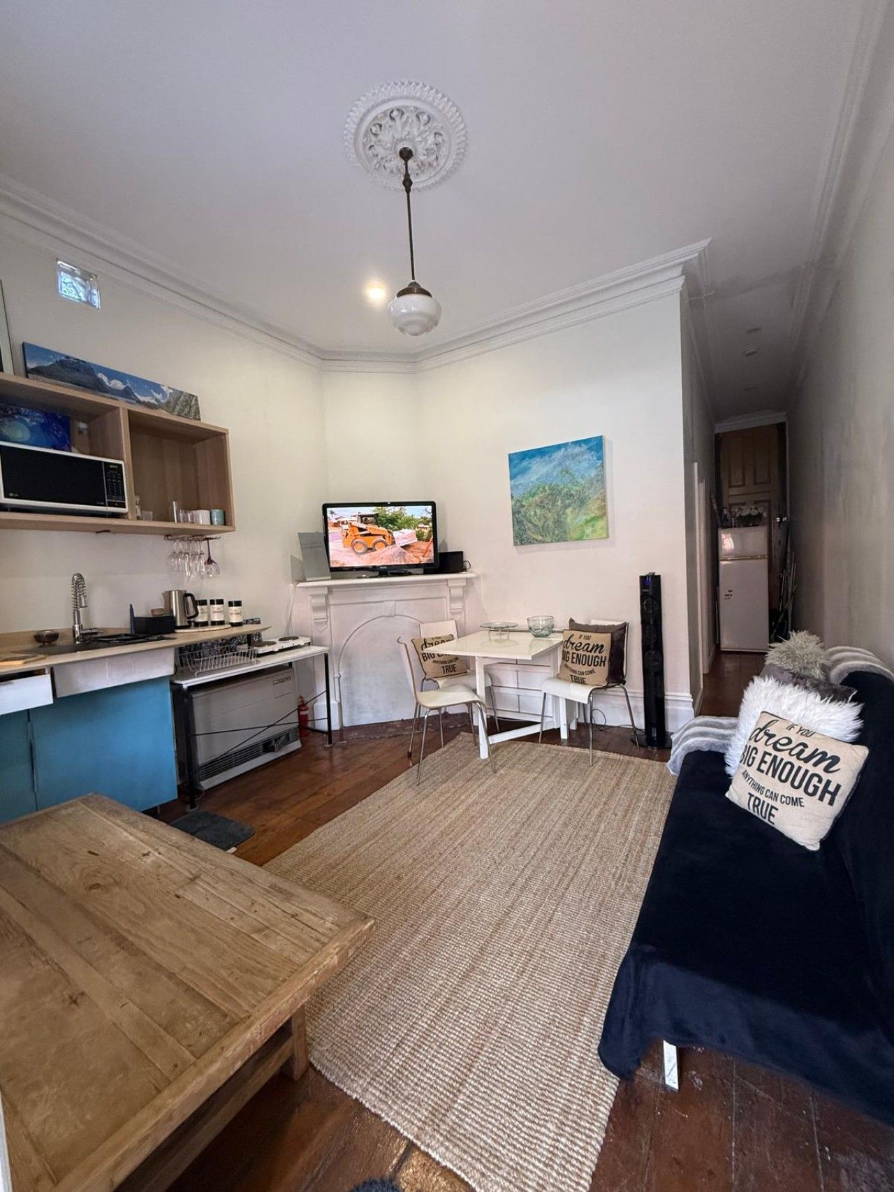 Een ruimtelijk ingerichte leefruimte met kitchenette, eethoek en een bed met een opbeurend kussen.
