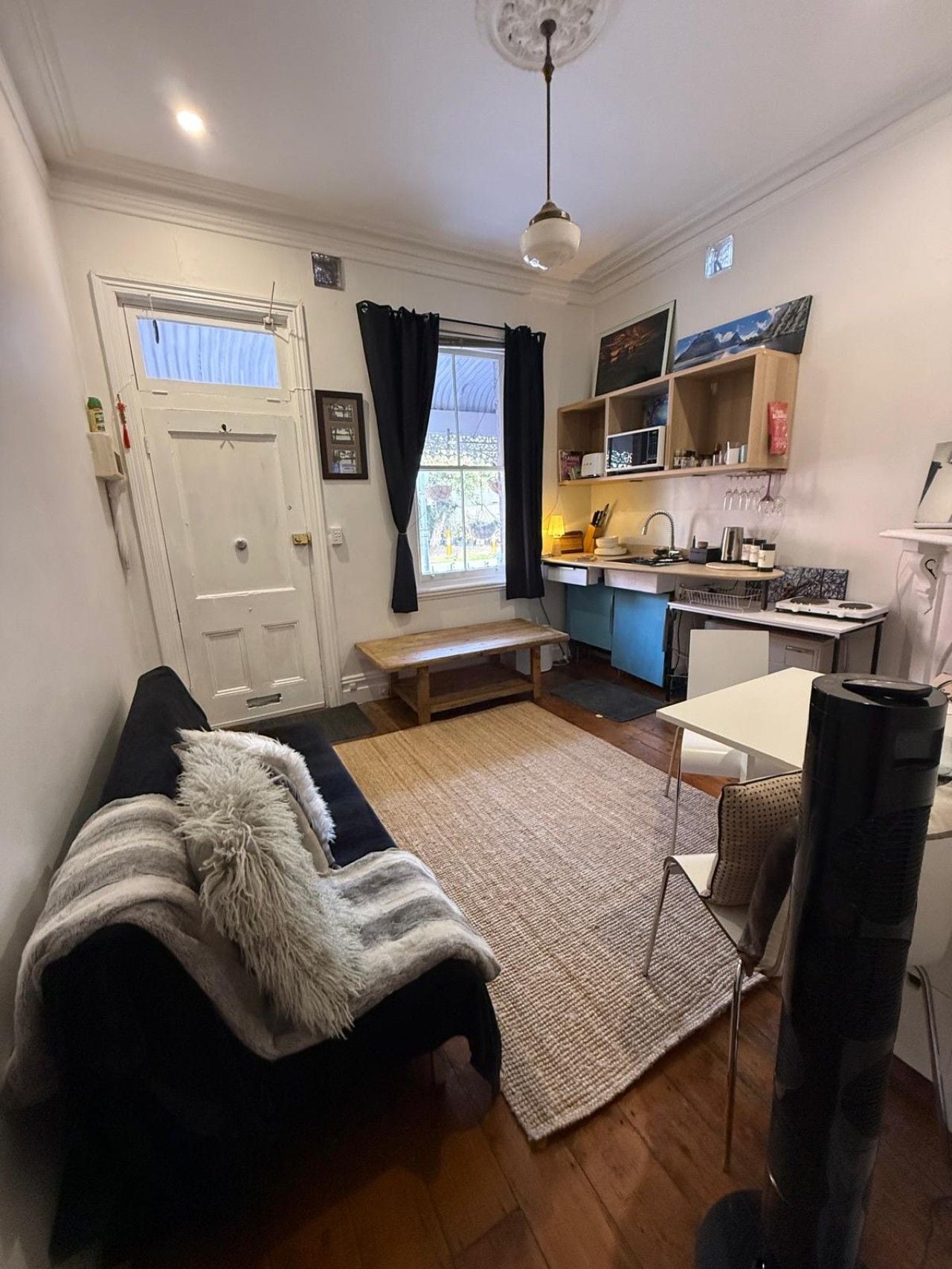 A compact living space with a sofa, a dining table, a kitchen area, and a window with curtains.
