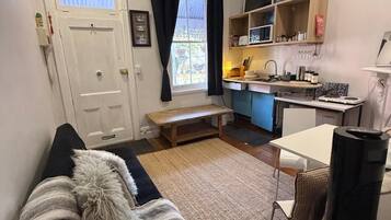 A compact living space with a sofa, a dining table, a kitchen area, and a window with curtains.