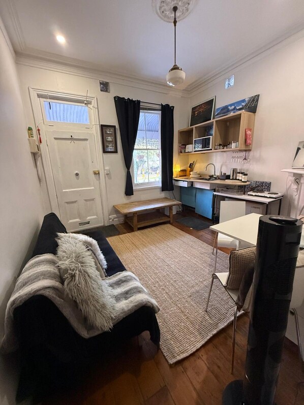 A compact living space with a sofa, a dining table, a kitchen area, and a window with curtains.