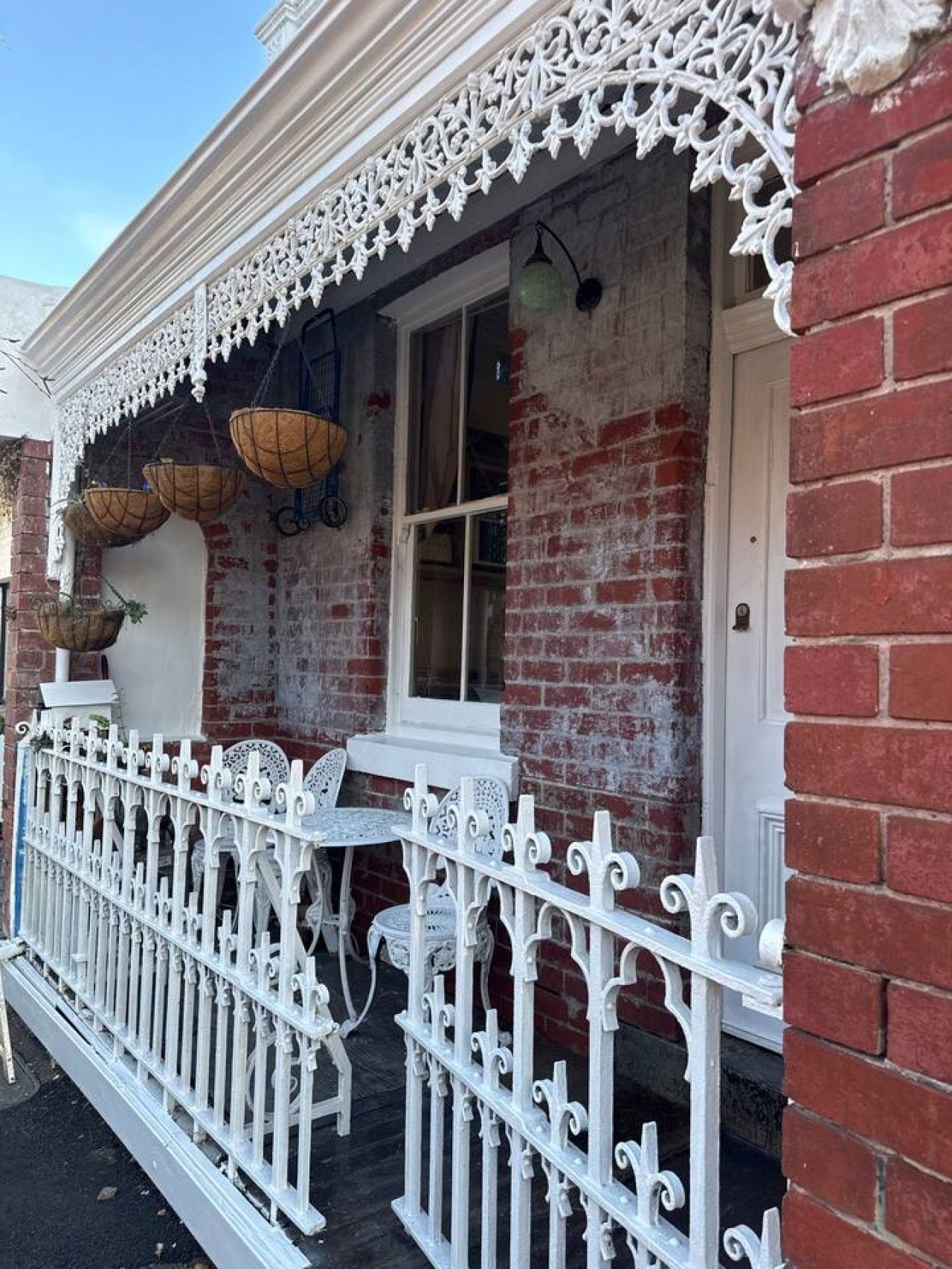 A building with a brick facade, white decorative railings, and hanging baskets.
