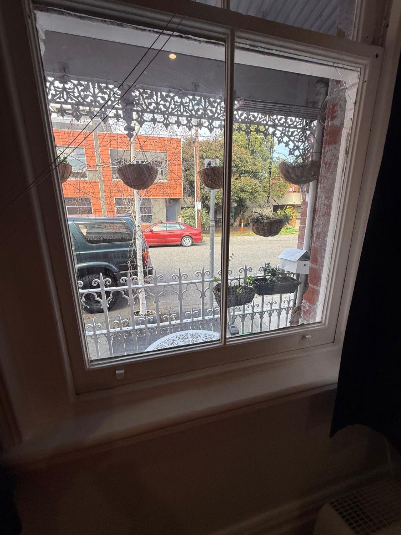 A window with a view of a street, a red car, and a black car parked outside.