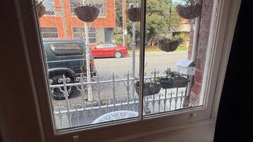 A window with a view of a street, a red car, and a black car parked outside.