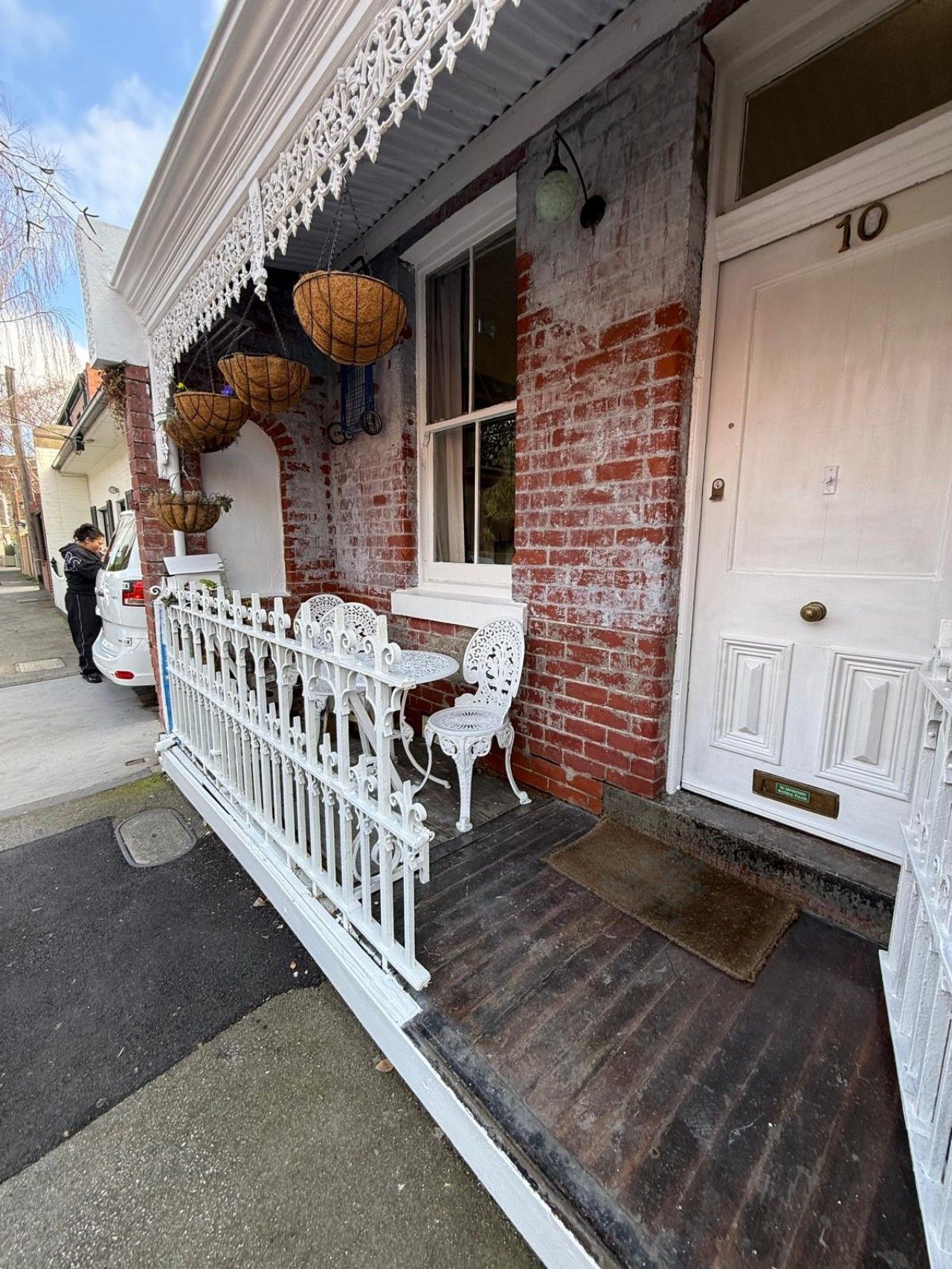 A building with a white door marked with the number 10, a brick facade, and a white picket fence.