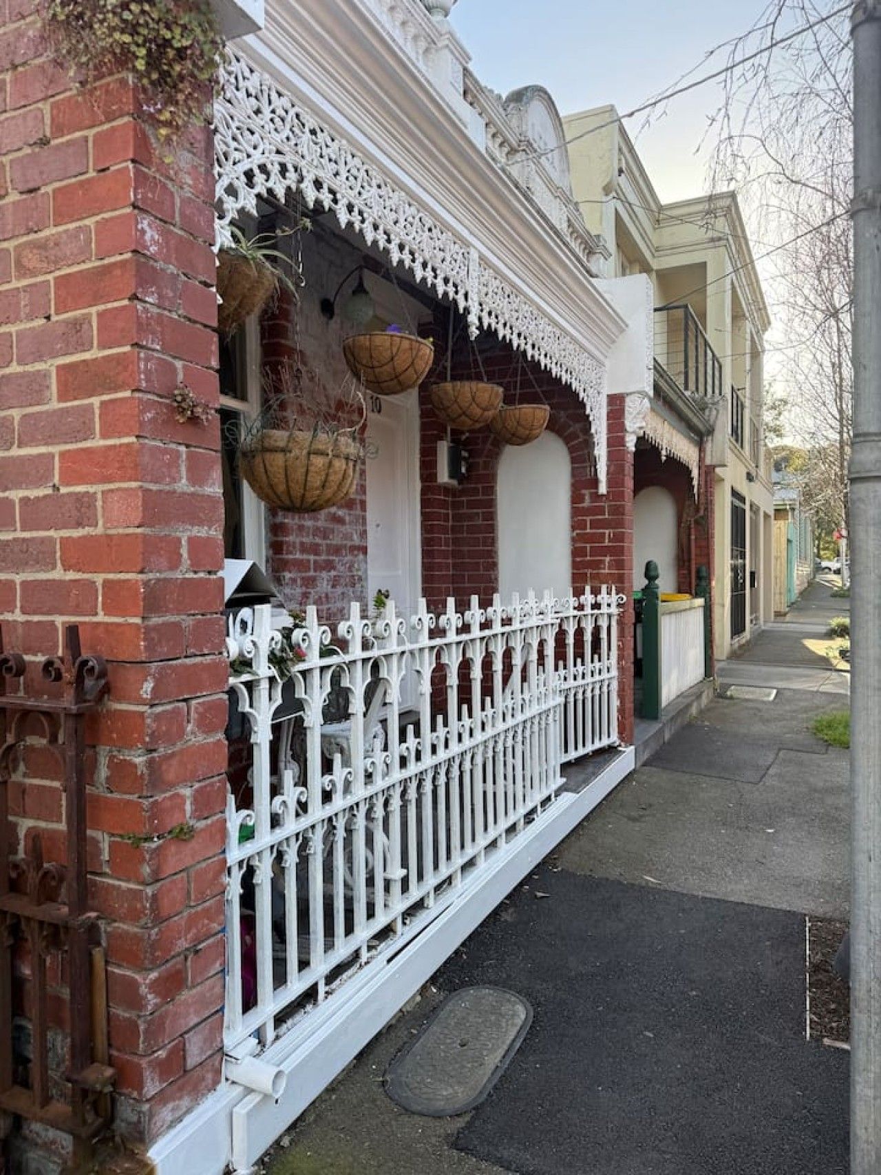 A brick building with a white decorative fence, a white door, and hanging baskets.
