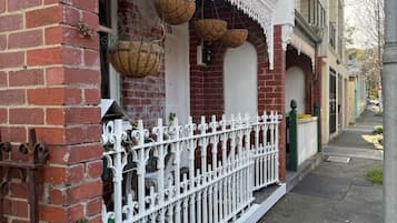 A brick building with a white decorative fence, a white door, and hanging baskets.