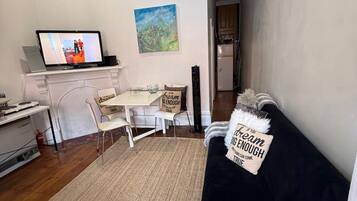 Uma sala de estar com um sofá preto, uma mesa de centro, uma TV em um suporte e um quadro na parede.