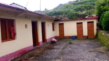 Un edificio con varias habitaciones, un patio de grava y una colina al fondo.