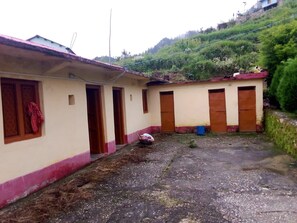 A building with multiple rooms, a gravel courtyard, and a hillside in the background.