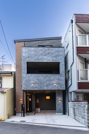 Un edificio moderno con entrada a garaje, un balcón visible en el piso superior y un cielo despejado.