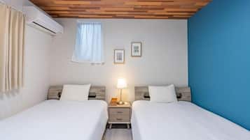 A hotel room with two beds, a ceiling with wooden panels, an air conditioning unit, a window with curtains, and two framed pictures on the wall.