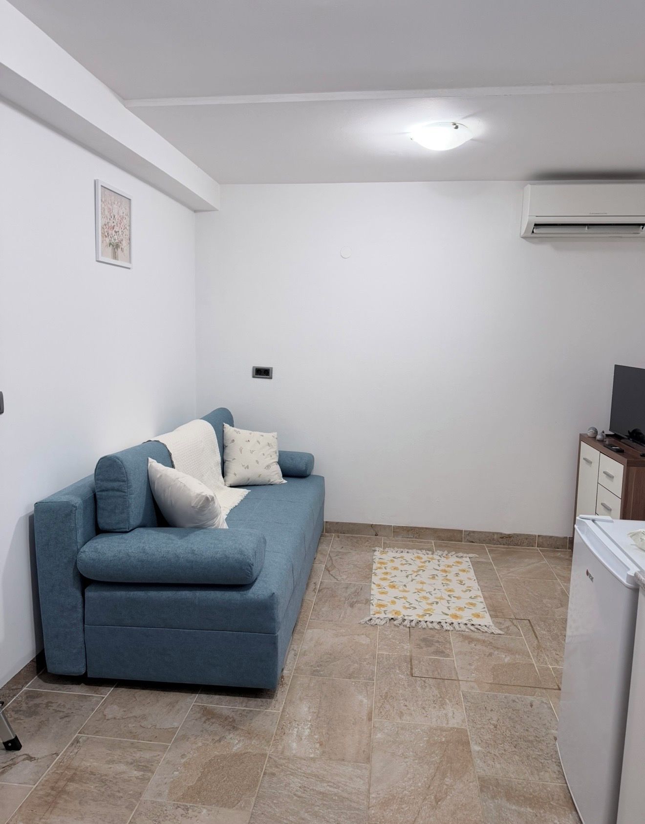 Un espace de vie compact avec un canapé bleu, un petit tapis et un réfrigérateur blanc.