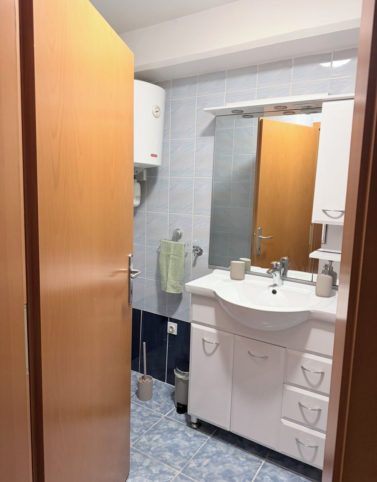 Une salle de bain avec un lavabo blanc, un miroir et un meuble, une serviette accrochée au mur et des toilettes.