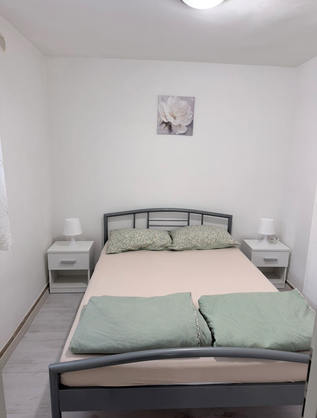 Un dormitorio con una cama, dos mesitas de noche, un cuadro en la pared y una lámpara en el techo.