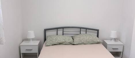 Un dormitorio con una cama, dos mesitas de noche, un cuadro en la pared y una lámpara en el techo.