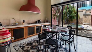 Cozinha com uma coifa vermelha grande, área de jantar com mesa posta para quatro pessoas e vista para uma piscina e vegetação lá fora.