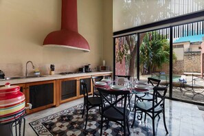 Een keuken met een grote rode afzuigkap, een eethoek met een tafel voor vier personen, en uitzicht op een zwembad en groen.