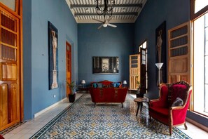 Ein Zimmer mit blauer Wand, einem roten Sofa, einem gemusterten Boden und Holztüren.