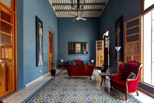 Una habitación con pared azul, sofá rojo, piso estampado y puertas de madera.